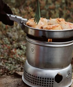 En person med sorte handsker steger kylling på en trangia og vender stykkerne med en grøn spork.